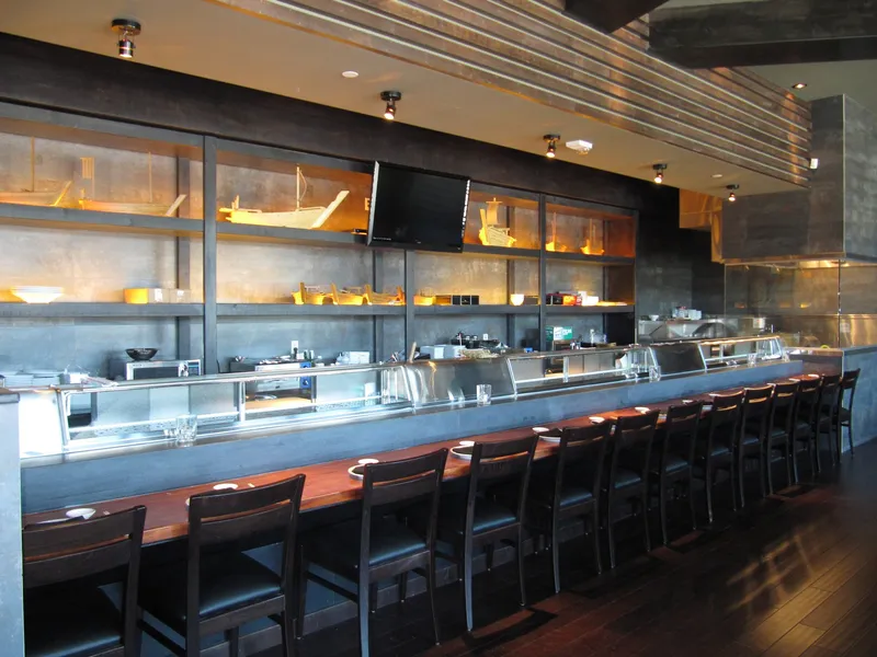 Wokcano bar counter lined with open refrigerated display cases and a stainless steel cook station
